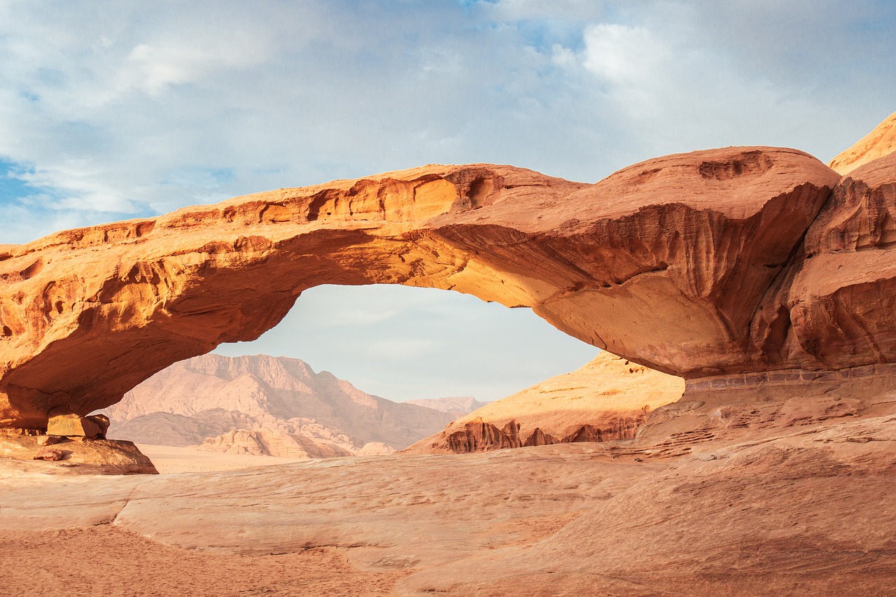 Panoramic view of Wadi Rum desert, featuring dramatic sandstone cliffs, expansive sand dunes, and a cloudless sky, highlighting the region's natural beauty.